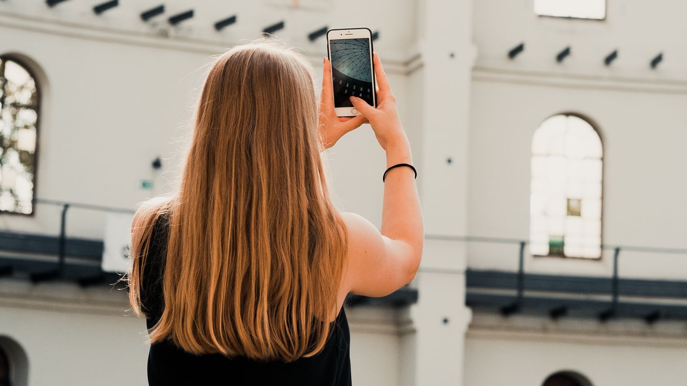 Eine Frau fotografiert mit ihrem Handy das Dach der Arena am Panometer. Beide Gebäude dienen als Ausstellungsraum für Kunst und sind Beispiele der Industriekultur in Leipzig