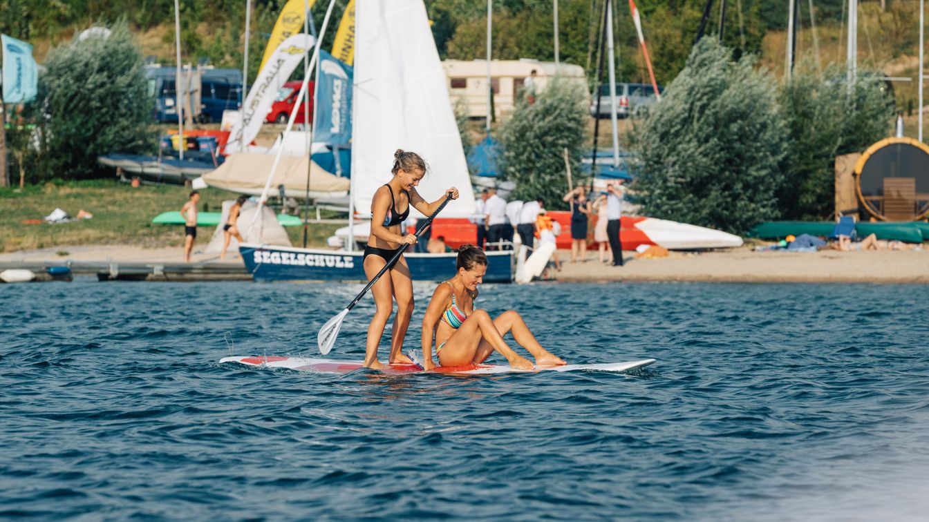 Zwei Frauen probieren Stand Up Paddeling auf dem See aus.