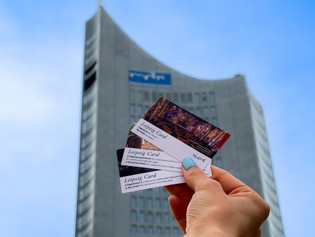 Eine Hand hält drei verschiedene LEIPZIG CARDS vor dem City-Hochhaus in Leipzig in die Luft