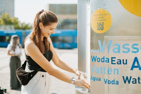 Eine Frau zapft an einem Trinkbrunnen Wasser. 