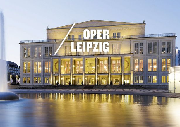 Vue de l'Opéra de Leipzig illuminé, derrière la fontaine de la place Augustusplatz, les drapeaux jaunes de l'Opéra annoncent le festival Wagner de Leipzig, ville de la musique.